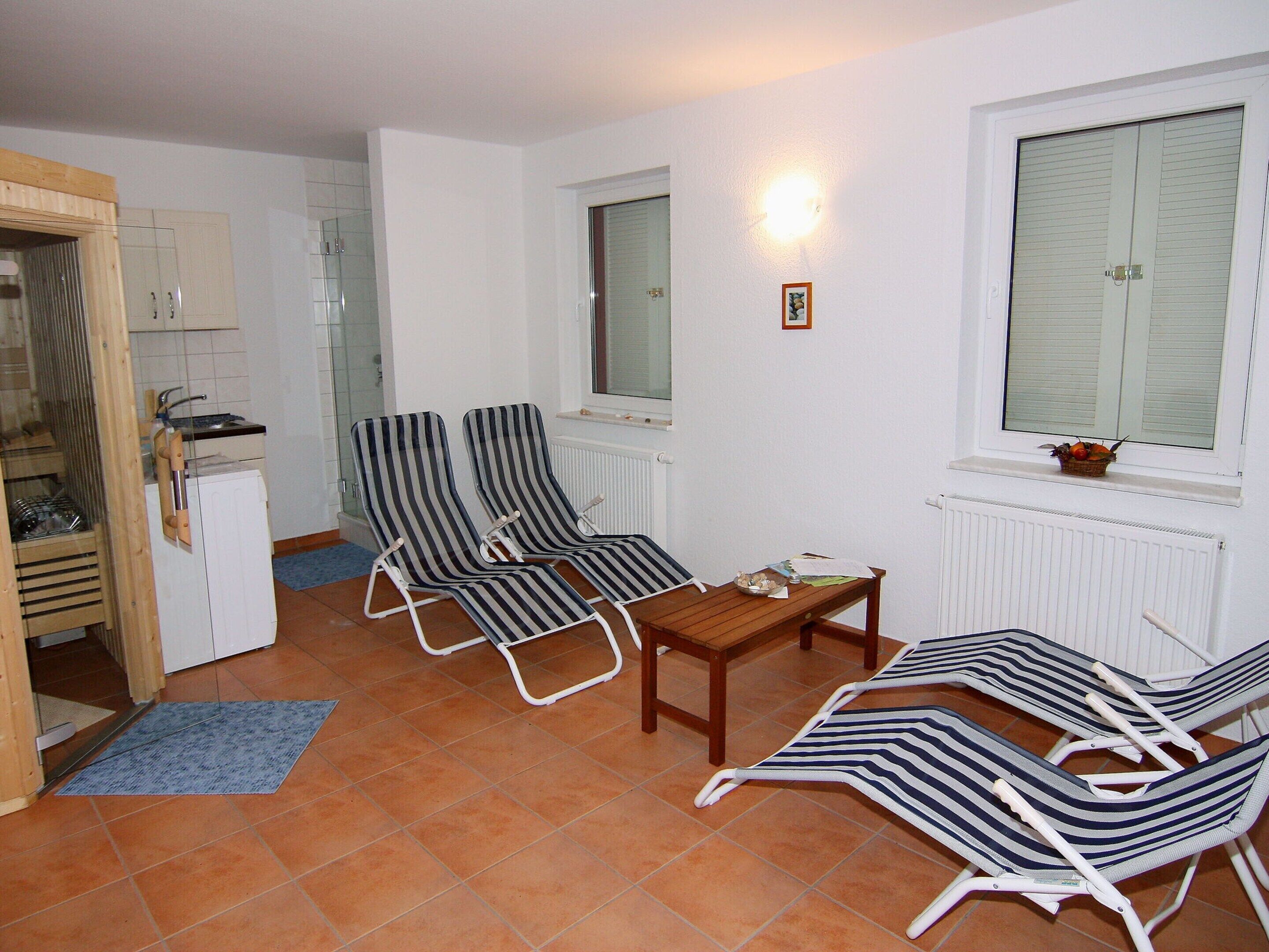 A compact living space with a kitchenette, two striped lounge chairs, a small wooden table, and a window with a view.