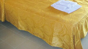 A bed with a yellow bedspread, two white towels, a wooden headboard, a nightstand, and a wall-mounted light.