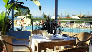 A dining table set with glassware and a pitcher, overlooking a pool area with lounge chairs and umbrellas.