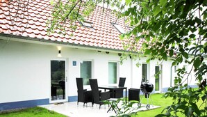 Uma casa com telhado de telhas, um pátio com mesa e cadeiras, e uma churrasqueira.