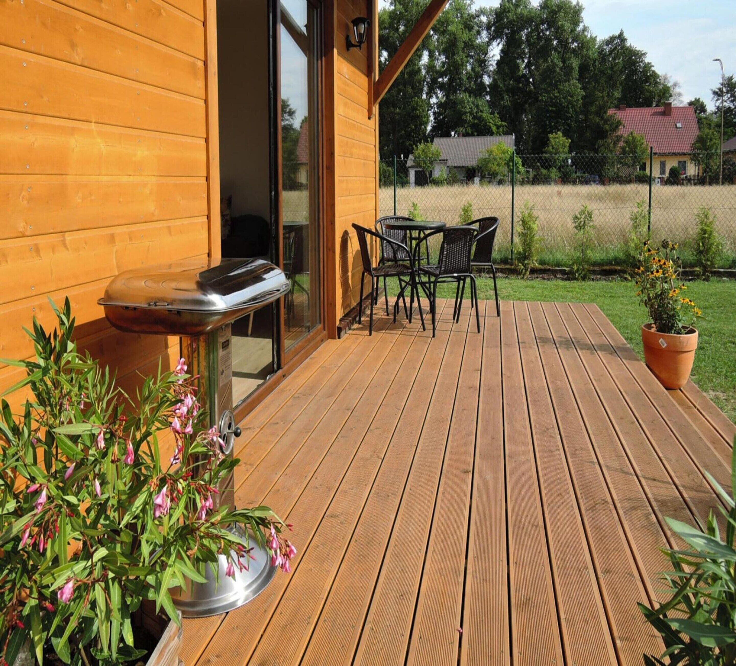 A wooden deck with a barbecue grill, outdoor chairs, and a potted plant.