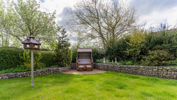A backyard with a stone wall, a wooden deck, and a barbecue area. - Ferienhaus mit Sauna in St.peter-ording (St. Peter-Ording)