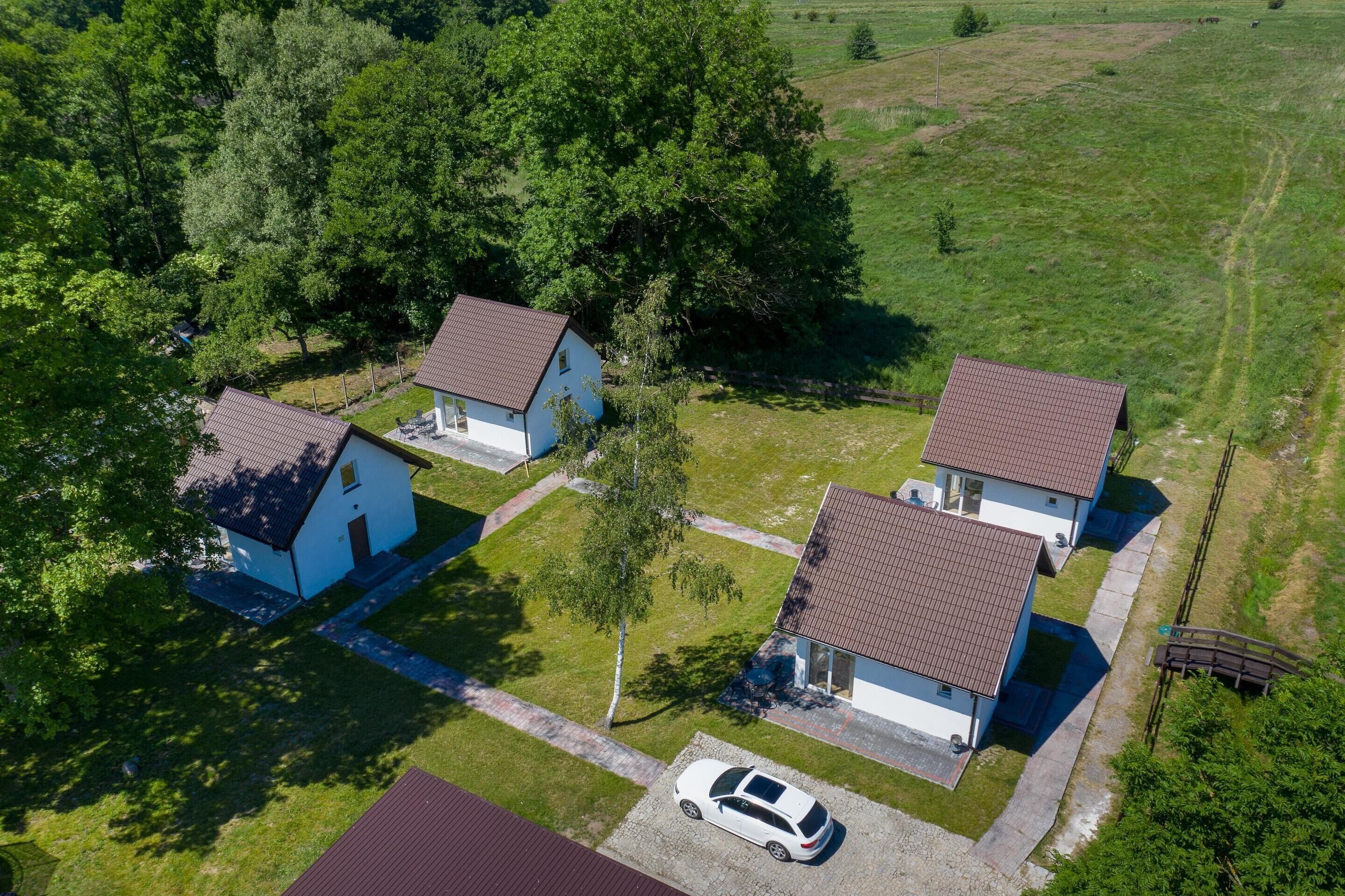 Ilmakuva asuinalueesta, jossa on kolme taloa. Jokaisella talolla on oma, selkeästi erottuva katon väri, ja talot ovat vehreän kasvillisuuden ympäröimiä, ja taivaalla on kirkasta.