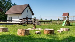 Une maison blanche avec un toit rouge, une balançoire en bois et un pont en bois dans un champ verdoyant.