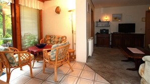 Un salon chaleureux, doté de meubles en osier, d’un téléviseur et d’un coin repas avec une table et des chaises.