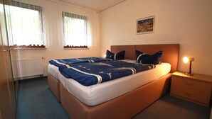 Une chambre avec un grand lit, une table de chevet, une fenêtre avec des rideaux et un tableau accroché au mur.