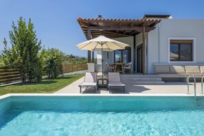 Un área de piscina con sillones de descanso y una sombrilla, un patio con mesa y sillas, y vistas del paisaje circundante.