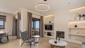 A modern living room with a flat-screen TV, a fireplace, and a dining area with a table and chairs. - Villa Wisdom (Chania)