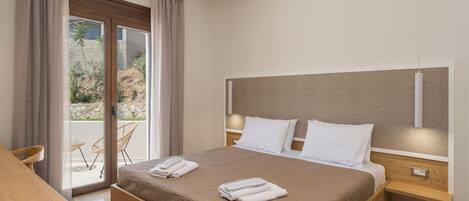 A modern hotel room with a large bed, a wooden nightstand, a desk, and a sliding glass door leading to an outdoor area.