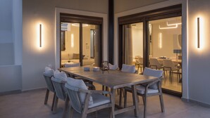 A modern dining area with a wooden table and chairs, surrounded by glass doors leading to another room. - Villa Wisdom (Chania)
