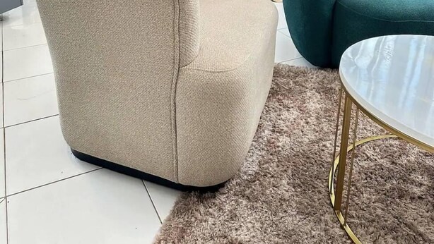 A living room with a beige armchair, a teal sofa, and a glass coffee table. - LivLuxe Apartments 6 (Kampala)