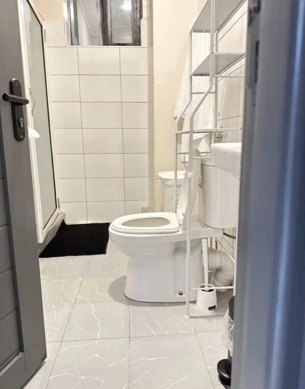 A bathroom with a toilet, a white sink, and a shower area. - LivLuxe Apartments 6 (Kampala)