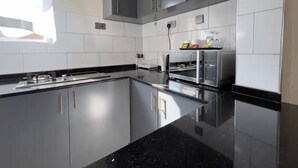 A modern kitchen with grey cabinets, a black countertop, and stainless steel appliances. - LivLuxe Apartments 6 (Kampala)