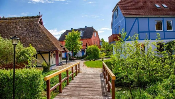 Un pont en bois mène à une rangée de maisons aux toits de chaume et à des immeubles modernes.