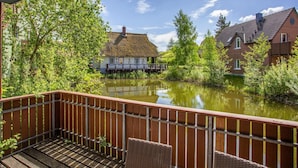 Une vue sur la rivière depuis un balcon doté de balustrades en bois, une maison à toit de chaume et une terrasse en bois avec des chaises.