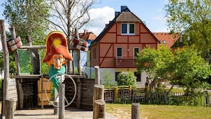 Une structure rustique en bois, avec une statue, une corde et une maison en arrière-plan.