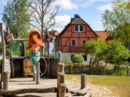 Una construcción rústica de madera con una figura, una cuerda y una casa al fondo.