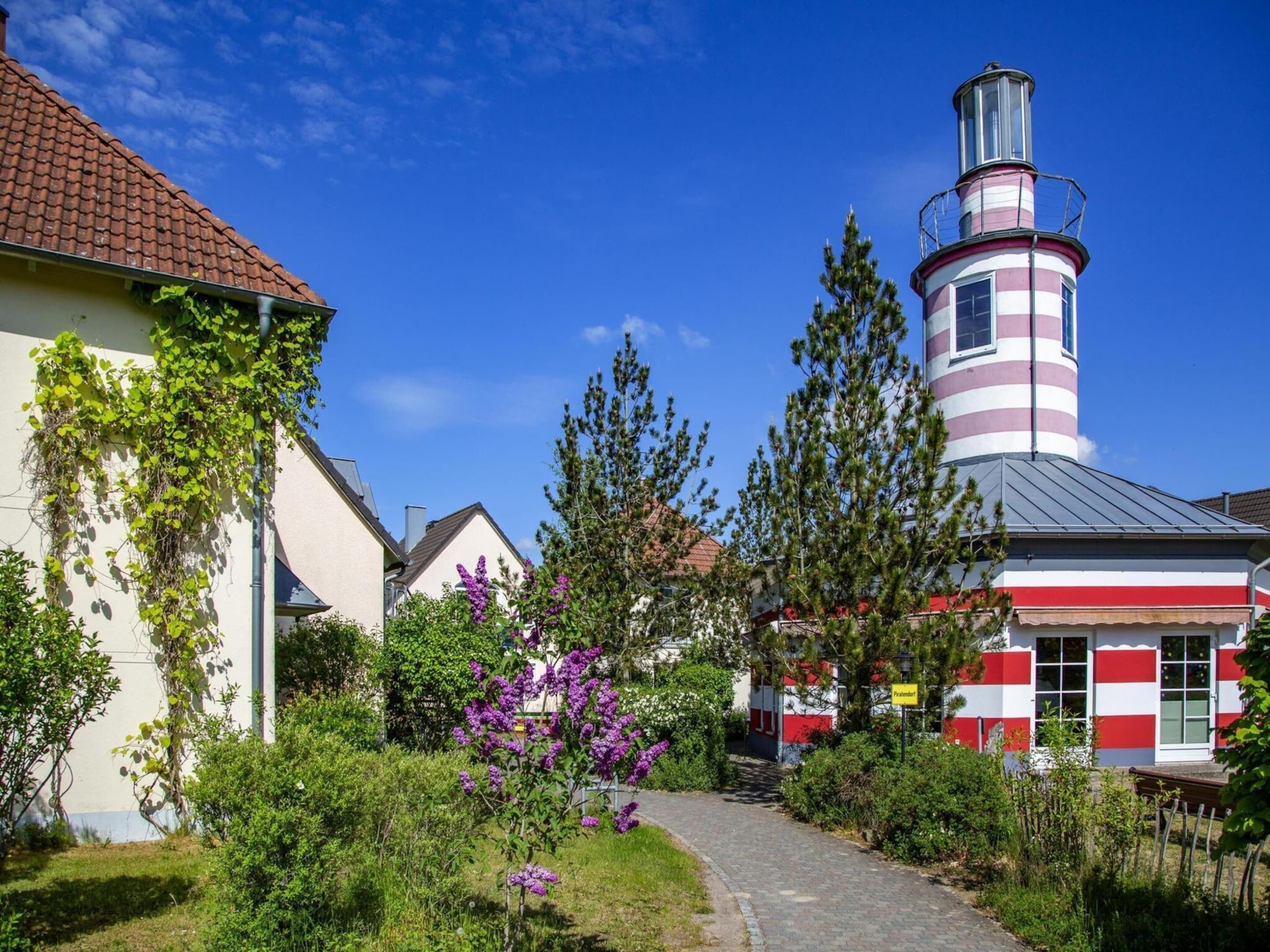 A lighthouse with a red and white striped tower, a pathway leading to it, and surrounding greenery.