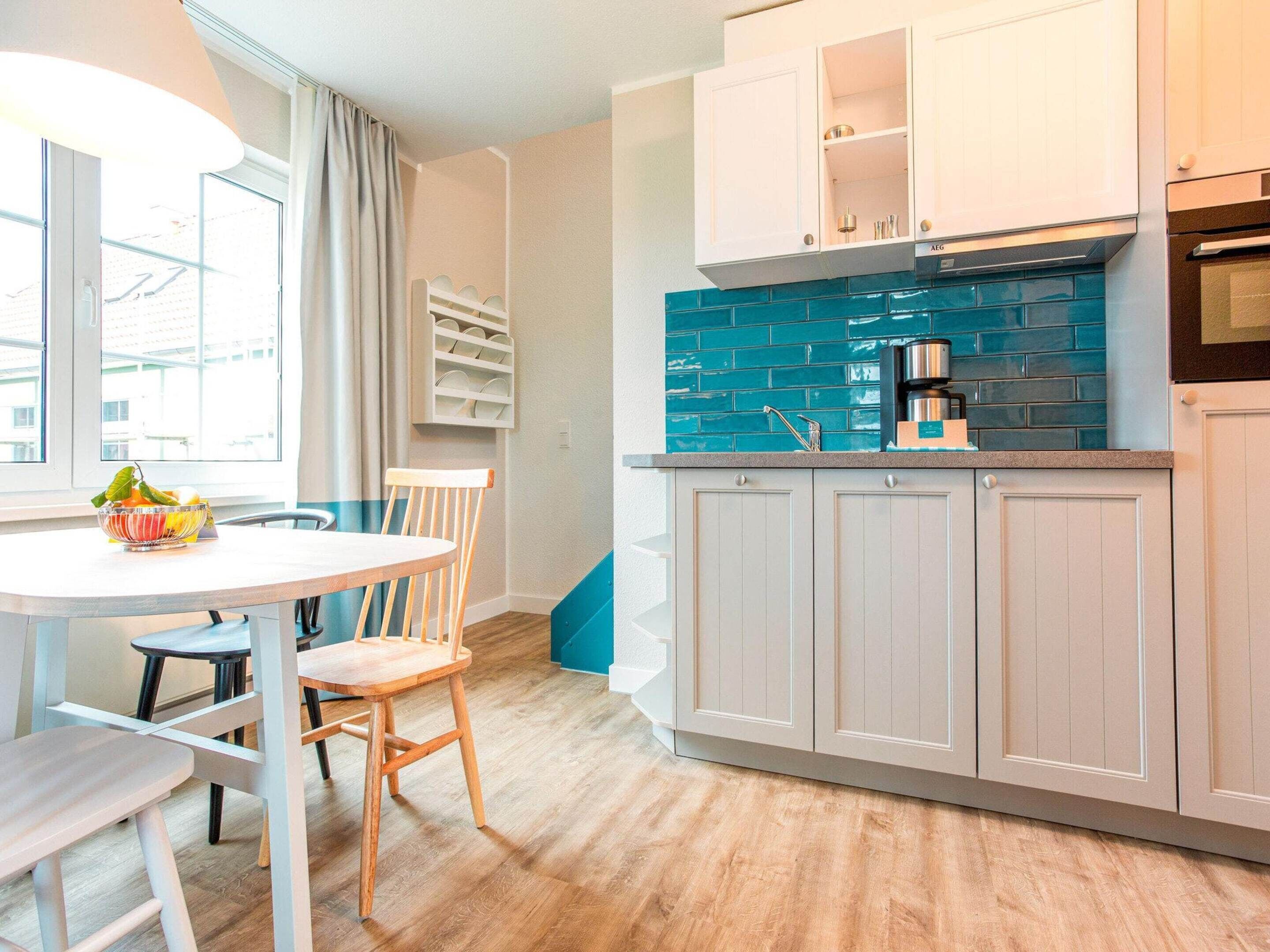 A modern kitchen with white cabinets, a blue backsplash, and a dining area with a table and chairs.