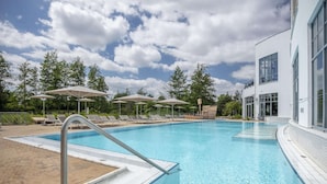 Une piscine entourée d’arbres et d’un bâtiment moderne, avec des chaises longues et des parasols.