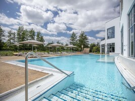 Una piscina con sillones de descanso y sombrillas, rodeada de árboles y un edificio moderno.