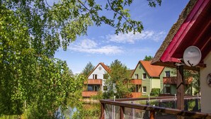 Un chalet au bord du lac, doté d’une terrasse en bois, d’un toit rouge et d’une antenne parabolique.