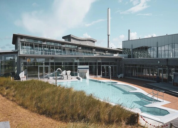A modern building with a large pool area, including a hot tub and lounge chairs. - Ferienwohnung in St. Peter-ording (St. Peter-Ording)