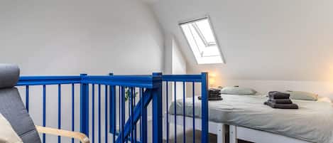 A bedroom with a skylight, a bed, a chair, and a blue railing.