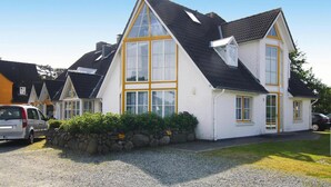 Une maison à deux étages, dotée d’un toit à forte pente, de grandes fenêtres et d’un mur en pierre à l’avant.