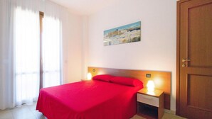 Una habitación de hotel con una cama, una mesita de noche con lámpara, una puerta y un cuadro en la pared.