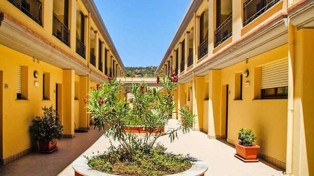 Un pasillo con paredes amarillas, plantas en macetas y un jardín central.