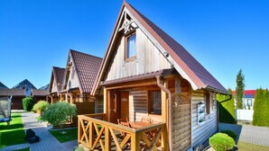 A wooden cabin with a porch, a small deck, and a garden area with rocks and plants. - Cottage in Ustronie Morskie Near Beach (Ustronie Morskie)