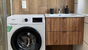 A modern bathroom with a washing machine, sink, and wooden cabinetry. - Apartment for 4 People Near the sea in Grzybowo (Kolobrzeg)