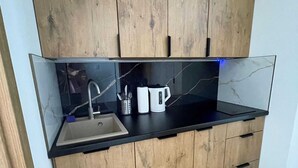 A modern kitchen with a black countertop, a sink, wooden cabinets, and a marble backsplash. - Apartment for 4 People Near the sea in Grzybowo (Kolobrzeg)