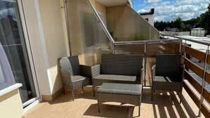 A balcony with wicker furniture, including chairs and a small table, and a glass door. - Apartment for 4 People Near the sea in Grzybowo (Kolobrzeg)