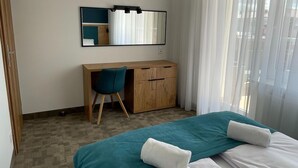 A hotel room with a bed, a desk, a chair, a wardrobe, and a large window with curtains. - Apartment for 4 People Near the sea in Grzybowo (Kolobrzeg)