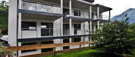 A multi-story building with balconies, a wooden fence, and a mountainous backdrop.