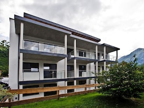 A multi-story building with balconies, a wooden fence, and a mountainous backdrop. - Apartment in Neukirchen by Wildkogelbahn (Neukirchen am Grossvenediger)