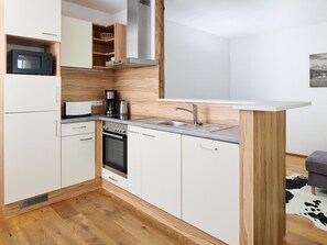 A compact kitchen with white cabinets, a built-in microwave, a stove, and a sink. - Apartment in Neukirchen by Wildkogelbahn (Neukirchen am Grossvenediger)