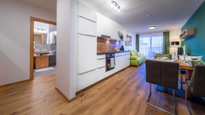 A modern kitchen with white cabinets, a wooden countertop, and a dining area with a table and chairs. - Apartment in Neukirchen by Wildkogelbahn (Neukirchen am Grossvenediger)