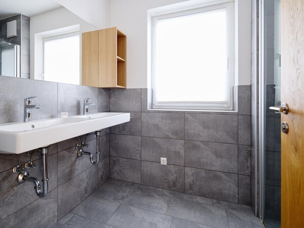 A modern bathroom with a white sink, wooden cabinet, and a shower area. - Apartment in Neukirchen by Wildkogelbahn (Neukirchen am Grossvenediger)