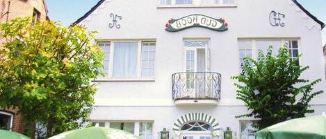 A white building with a sign reading "GOLD HOUSE" and a balcony. There are green umbrellas in front.