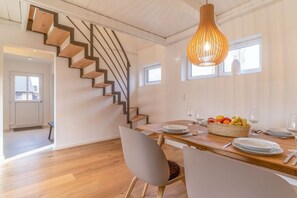 Un comedor moderno con una escalera de madera, una mesa de comedor de madera dispuesta con platos y vasos, y un colgador de luz.