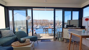 Un salon moderne avec un canapé, une table basse, un téléviseur et une vue sur un port de plaisance.