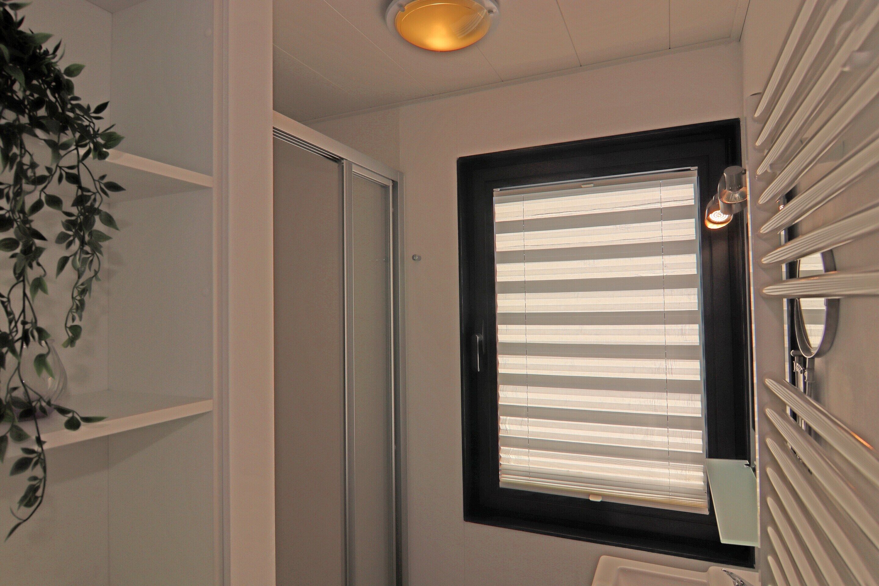 A bathroom with a white door, a window with horizontal blinds, a towel rack, and a potted plant.
