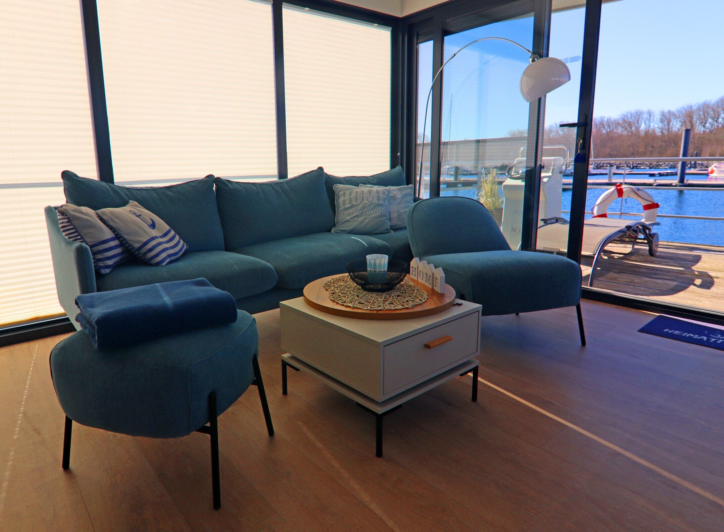 A modern living room with a sofa, two armchairs, a coffee table, and a large window offering a view of a body of water.