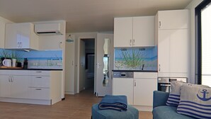 Un espace de vie compact comprenant un coin cuisine, un coin repas et un coin salon agrémenté de coussins sur le thème de la marine.