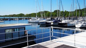 Un port de plaisance où sont amarrés plusieurs voiliers, une terrasse en bois et un petit bâtiment aux fenêtres en verre.