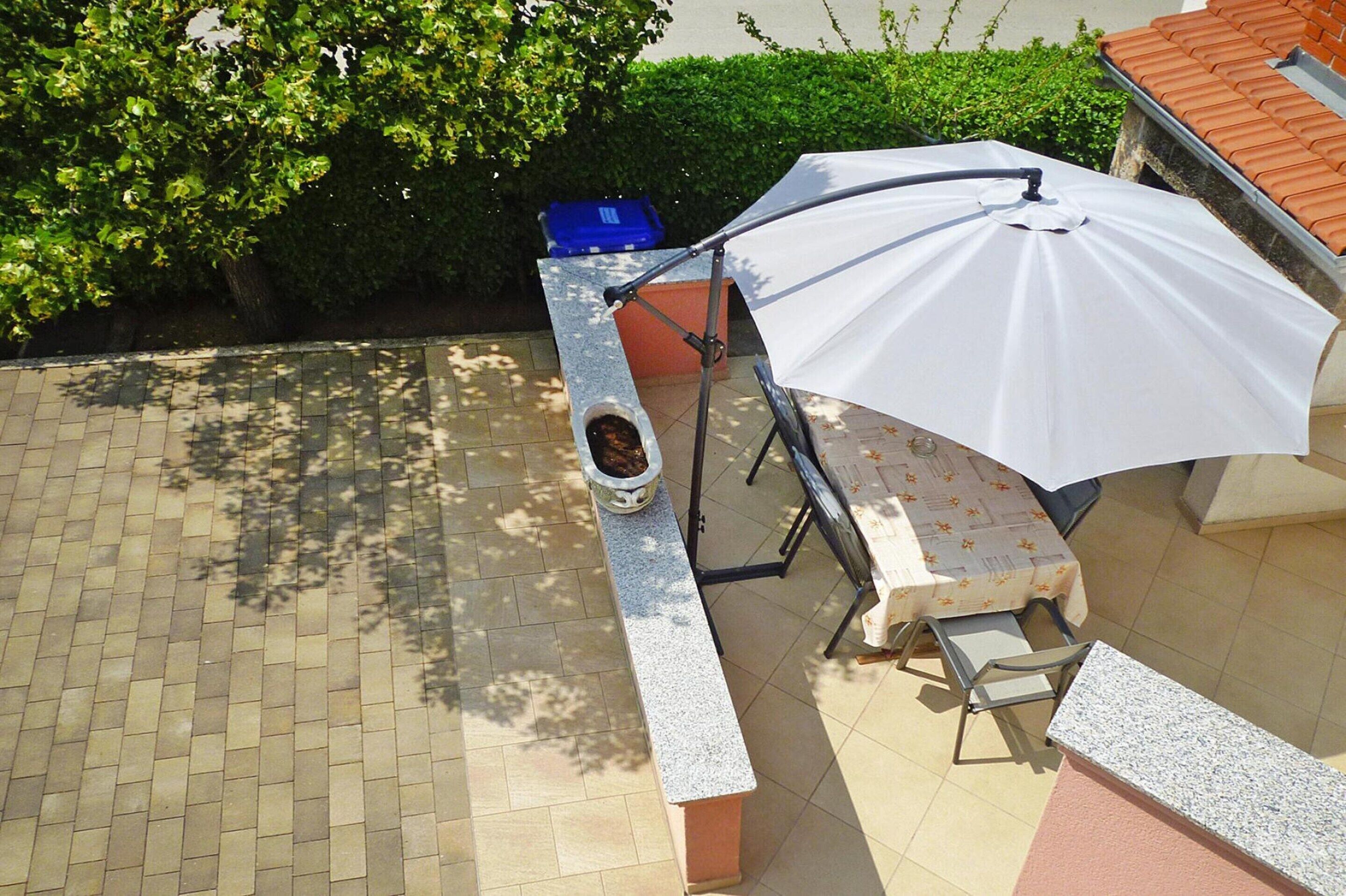 A patio area with a table, chairs, a white umbrella, and a stone bench.