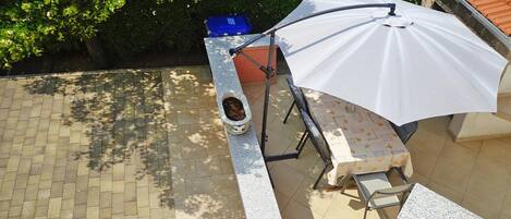 A patio area with a table, chairs, a white umbrella, and a stone bench.